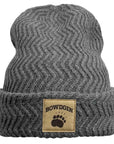 A dark gray ribbed knit beanie hat with a folded cuff, featuring a tan rectangular patch on the front with the word 'BOWDOIN' and a black paw print.