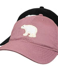 A dusty pink baseball cap featuring an embroidered white polar bear on the front, layered over a black baseball cap, shown against a plain white background.