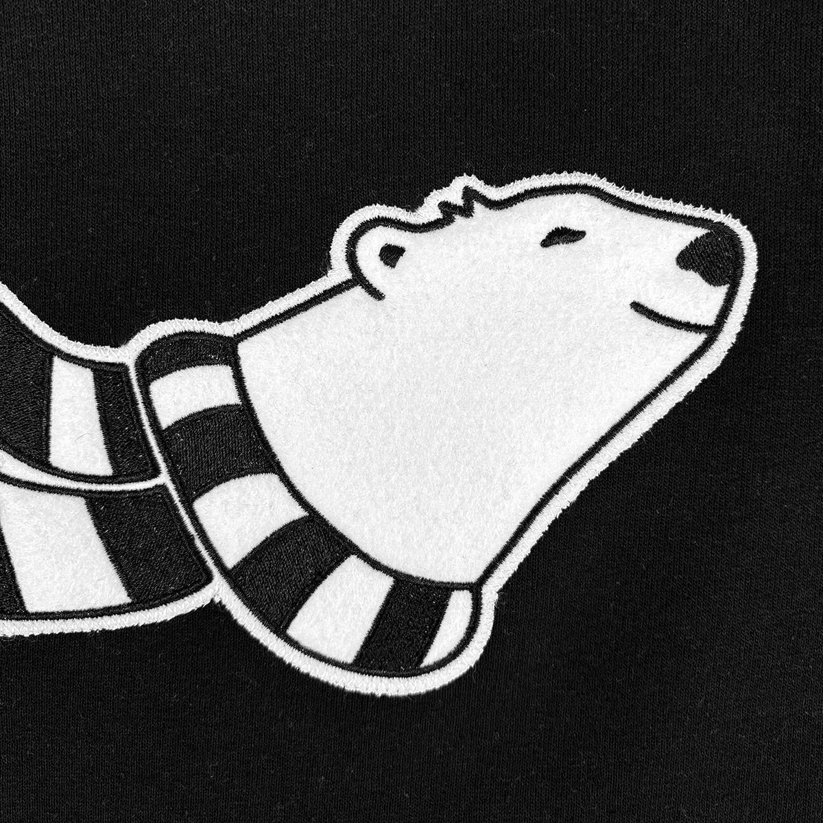Detail of cartoon polar bear with a striped scarf applique on black fabric.