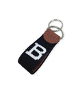 A black needlepoint key fob with a large white letter 'B' and a brown leather patch embossed with 'S&B', attached to steel key rings on a white background.
