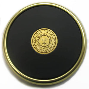 Round black leather coaster with gold rim and gold engraved Bowdoin sun seal in center.