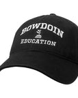 Black ball cap with white embroidery of BOWDOIN arched over a plant growing out of a stack of books over EDUCATION