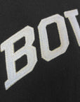 A closeup view of the letters BOW embroidered on the chest of a black sweatshirt, showing the texture of the reverse weave sweatshirt and the quality of the stitching in the ivory thread and felt of the letters.