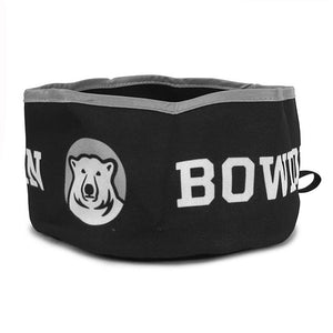 Open fabric dog bowl, in black with white repeating BOWDOIN and polar bear medallion imprint. Grey piping around top.