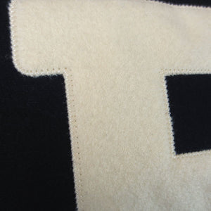 A closeup of the embroidered ivory felt B on the chest of a black sweatshirt, showing the quality and texture of the embroidery.