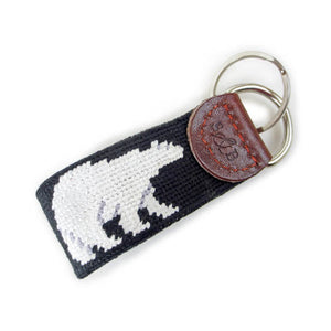 Needlepointed keyfob decorated with a white polar bear on a black background. Small leather tab at the end attaching the metal key ring, debossed with the S&B logo.