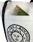 Closeup showing a postcard poking out of the pocket of a Bowdoin seal tote bag.