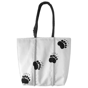 White tote with black rope handle and trail of paw prints leading from the bottom left corner to the top right.
