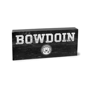 Grey wooden block with distressed imprint of BOWDOIN in white over a black, white and grey mascot medallion.