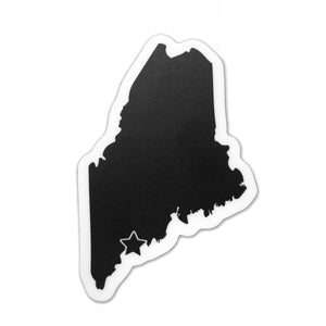 White sticker with black imprint of the state of Maine with a star over the map location of Brunswick.