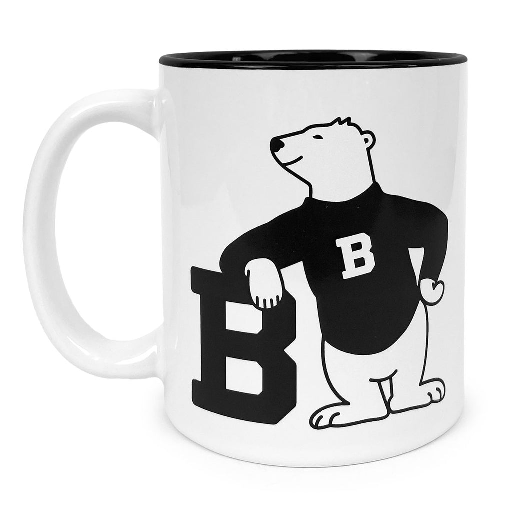 White coffee mug with black interior and cartoon polar bear imprint. Bear is wearing a black sweater with a white B on it, and leaning on a large black B.