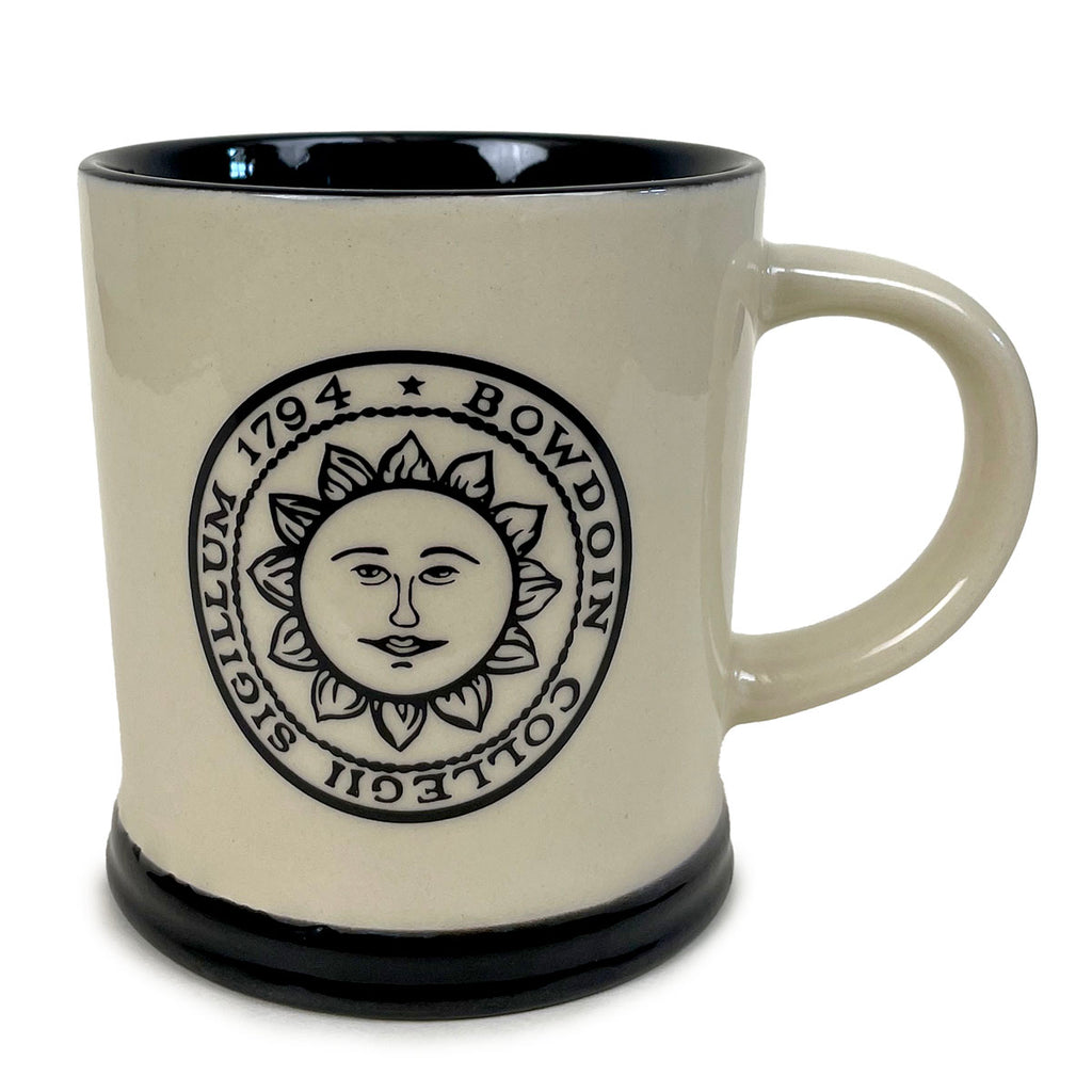 Tan mug with sides slightly tapered towards a flared black base. Black interior and imprint of Bowdoin College sun seal.