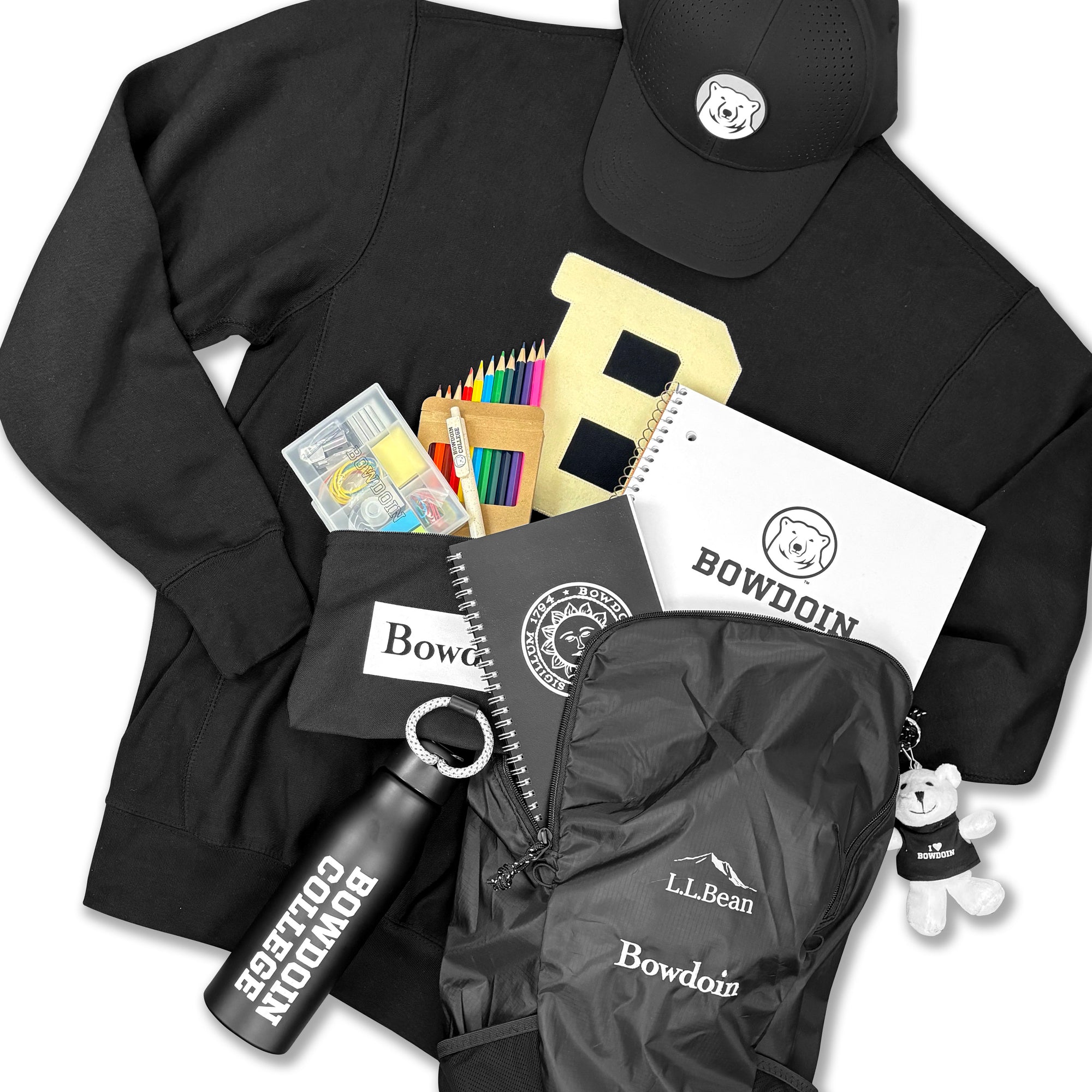 A flat-lay bundle of black collegiate apparel and accessories, including a sweatshirt, baseball cap, jacket, notebook, water bottle, pencil case, and small plush keychain, all featuring Bowdoin.
