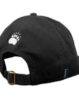 A black cotton baseball cap shown from the back, featuring a white embroidered bear paw print on the back and an adjustable black back strap with a brass buckle.