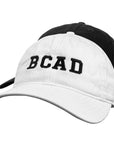 Stacked white and black baseball caps embroidered with BCAD on a white background.