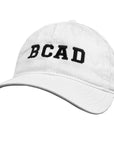 White baseball cap with BCAD embroidered on the front in black.