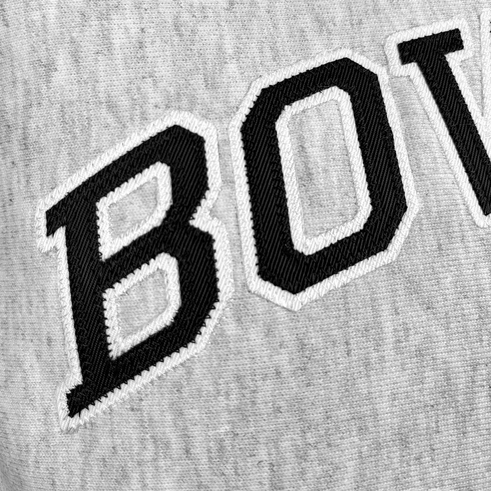 Close-up of a gray sweatshirt with 'BOW' embroidered twill letters in black and white on a textured fabric background