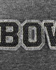Close-up of a dark gray heather knit fabric with a large embroidered patch reading "BOW" in black letters outlined in white and light gray.