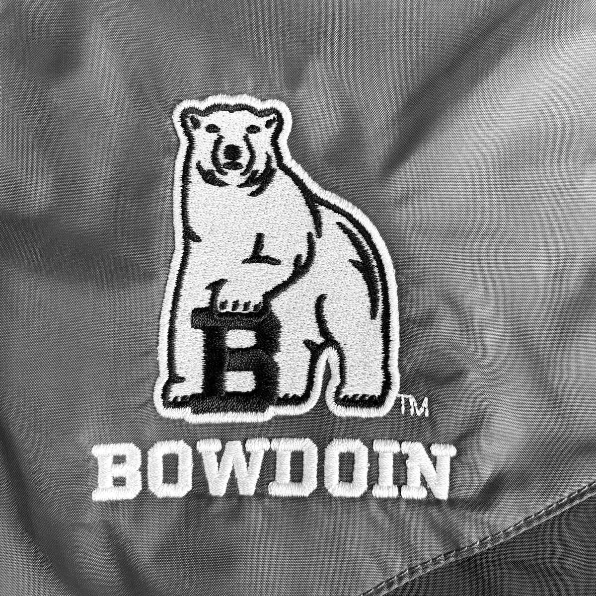Close-up of an embroidered Bowdoin bear logo with a large black letter B on a gray fabric background.
