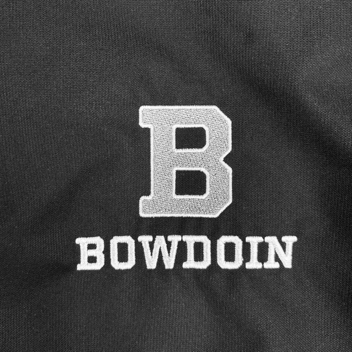 Close-up of a black fabric surface with a large white embroidered letter B above the word BOWDOIN in white embroidered block letters.