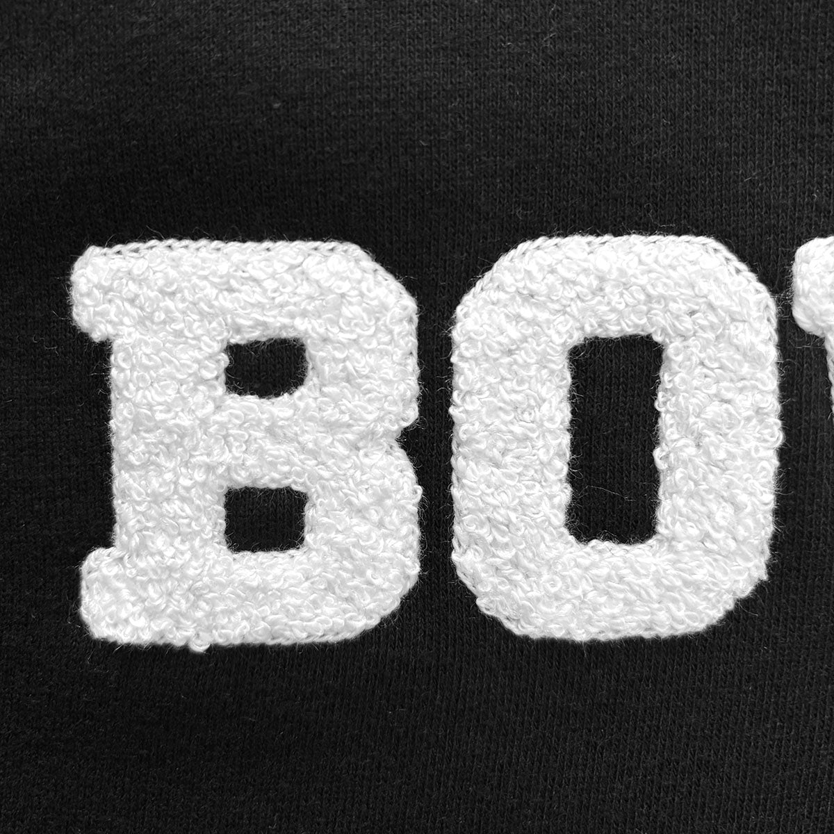 White chenille letters spelling 'BOW' on black sweatshirt fleece.