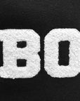 White chenille letters spelling 'BOW' on black sweatshirt fleece.