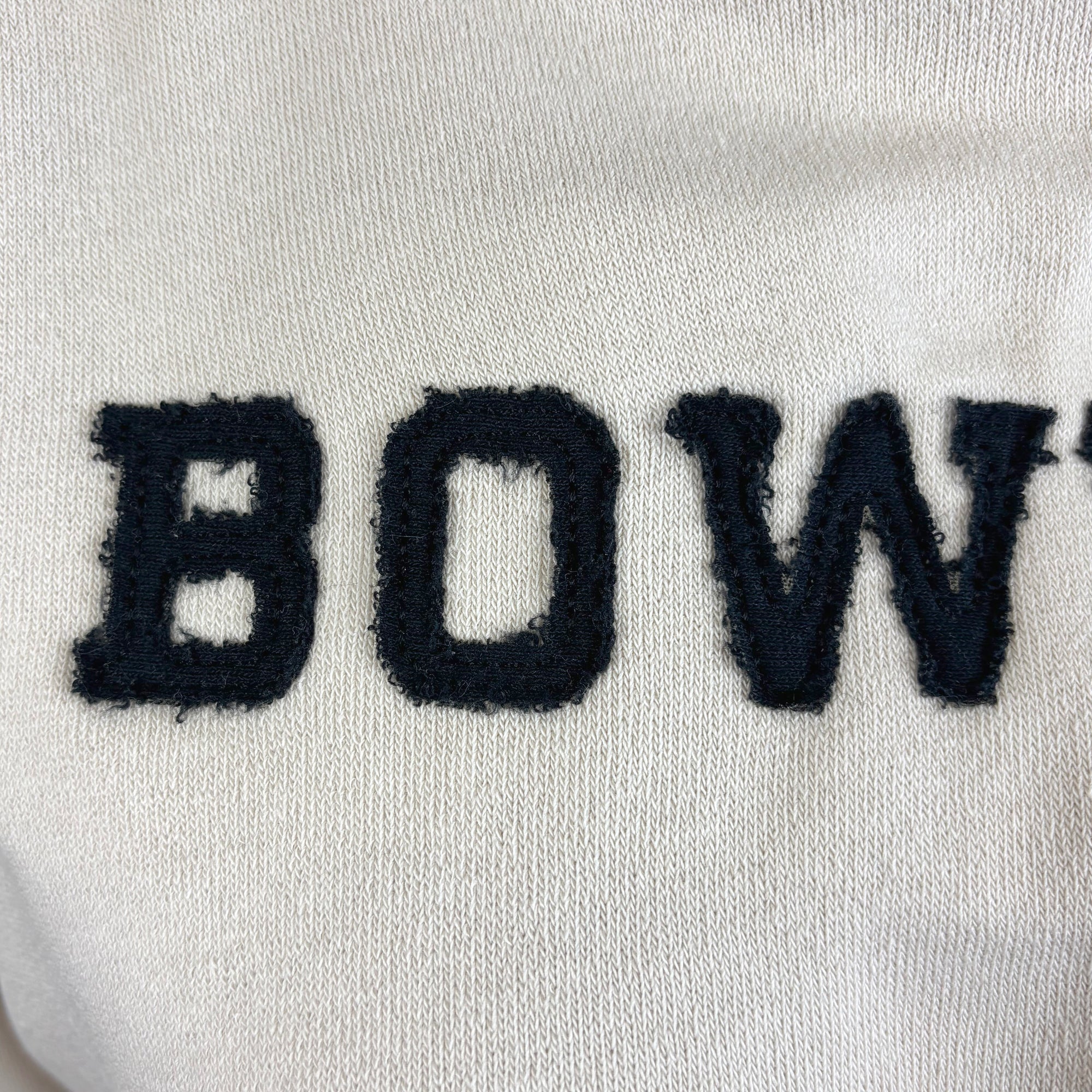 Close-up of a beige shirt with black BOW applique in unfinished fabric.