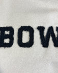 Close-up of a beige shirt with black BOW applique in unfinished fabric.