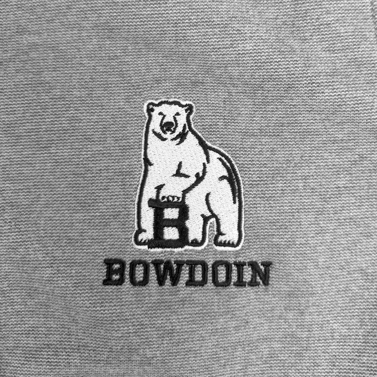 Close-up of a gray fabric surface featuring a white embroidered polar bear graphic with a black outlined letter B and the word BOWDOIN below it.