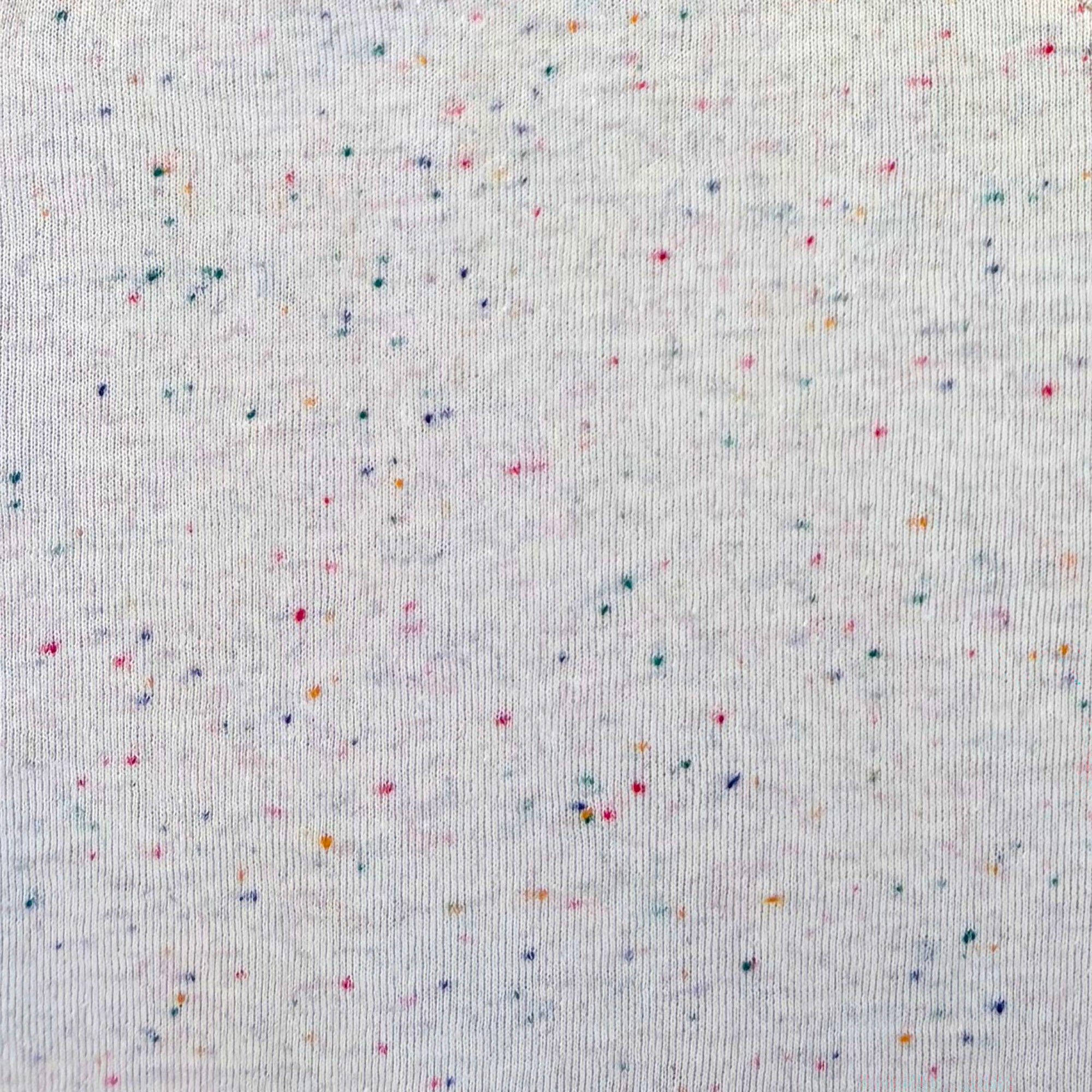 A close-up of an off-white knit fabric with a scattered confetti speckle pattern in multiple colors including pink, blue, orange, and green.