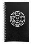 A black spiral-bound notebook with a white circular sun face emblem and the text 'BOWDOIN COLLEGII SIGILLUM 1794' printed on the cover, shown on a plain white background.