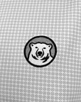 Closeup of embroidered medallion on polo chest, also showing detail of fabric print of many small diamonds with small dots in the center and one small line emerging from the center of each side of the diamond.