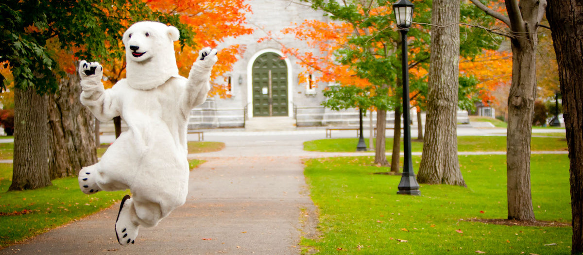Polar bear mascot jumping for joy in front of the Chapel at Bowdoin College. Fall leaves are beginning to turn orange.
