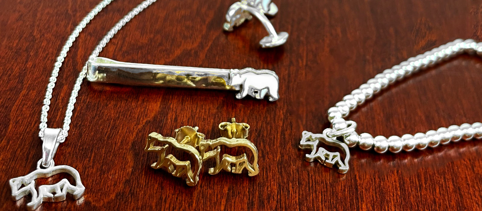 Photo of several pieces of gold and silver Bowdoin polar bear jewelry on a piece of mahogany colored wood.