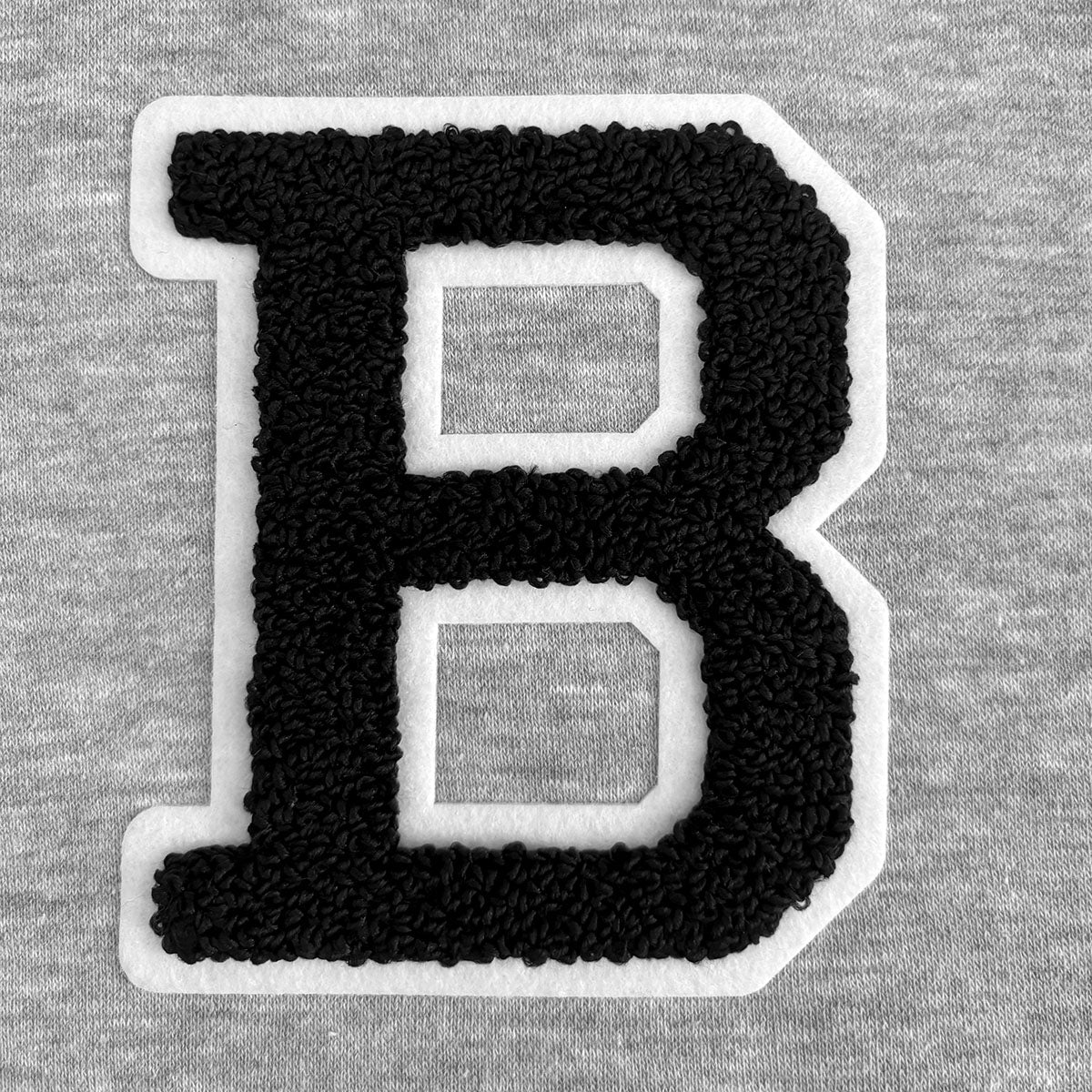 Letter 'B' patch in black chenille with a white felt outline on a gray sweatshirt material.