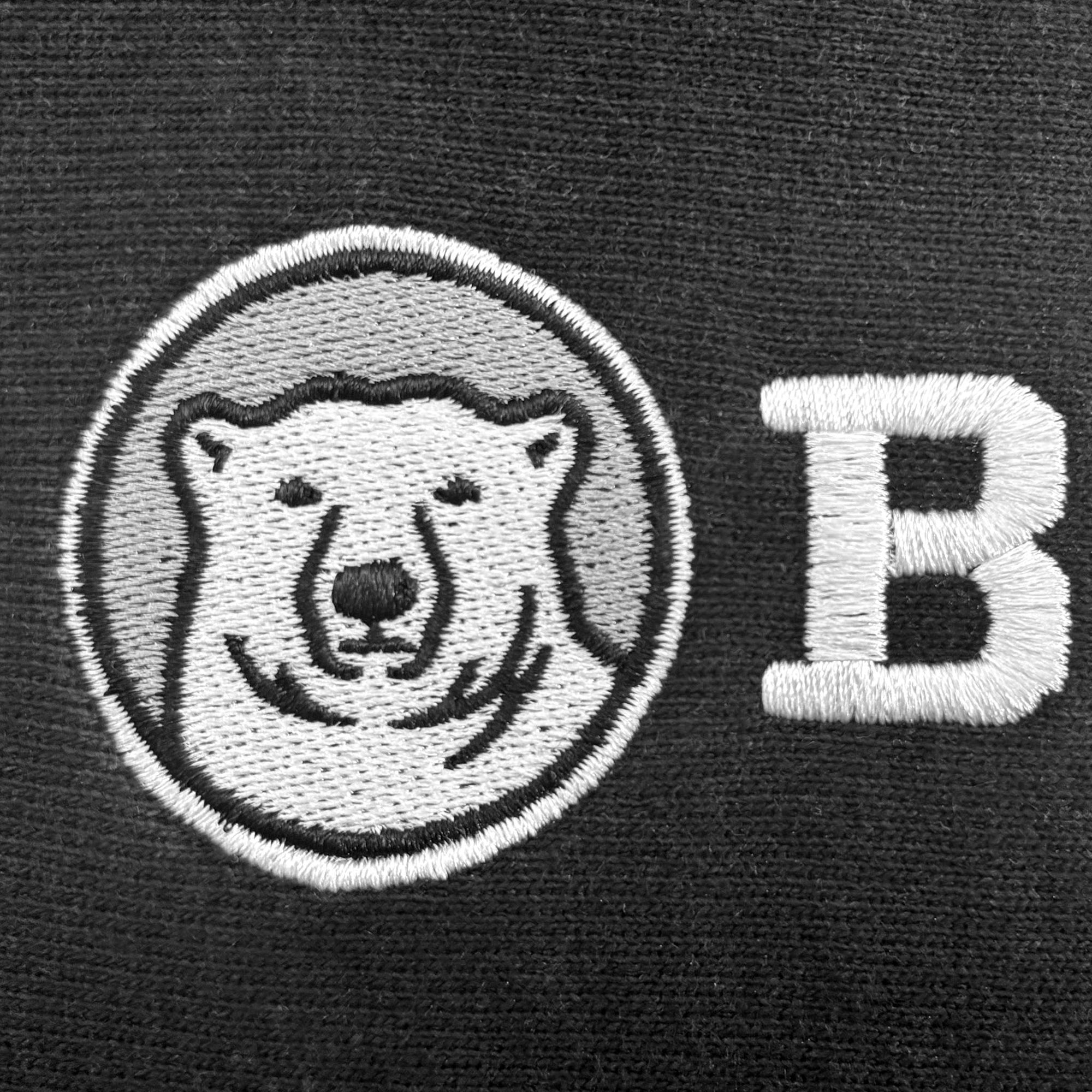 Close-up of a black knit fabric featuring a white embroidered polar bear face inside a circular patch and a large white embroidered letter B.