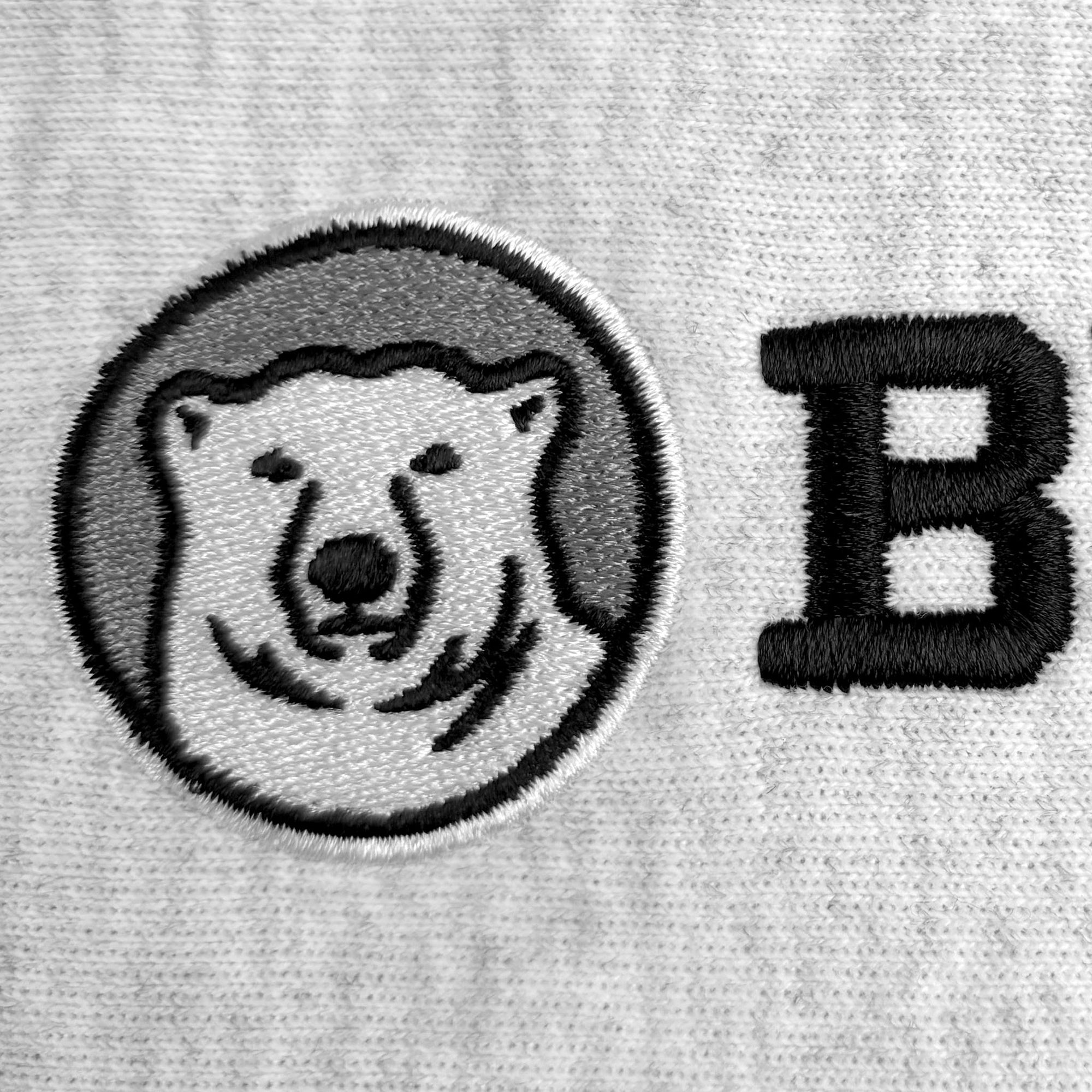 Close-up of a light gray embroidered fabric featuring a circular polar bear patch with black and gray embroidery, alongside a large black embroidered letter B.