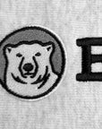 Close-up of a light gray embroidered fabric featuring a circular polar bear patch with black and gray embroidery, alongside a large black embroidered letter B.