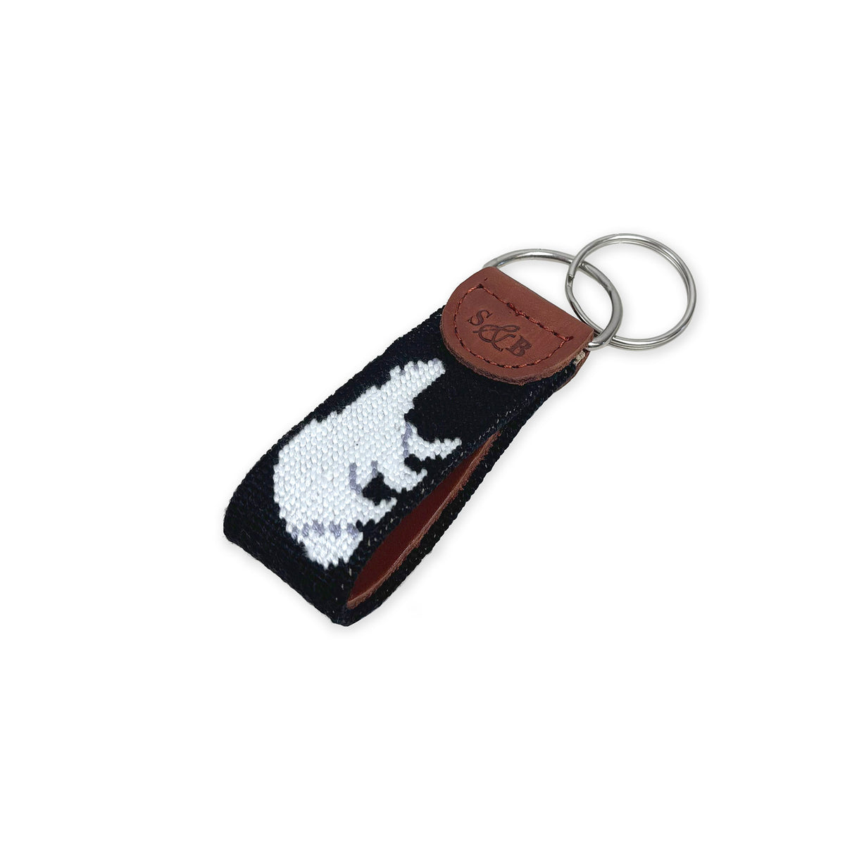 A black needlepoint key fob with a design of a white polar bear with a brown leather tab featuring the brand name 'S&amp;B', attached to two steel key rings, shown on a plain white background.