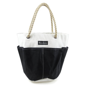 White bucket bag with black canvas exterior pockets. Natural rope handles. Black and white BOWDOIN wordmark patch on front.