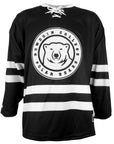 Black hockey jersey with white collar, white laces at throat, double white stripes on arms and lower torso. Large white patch applique with black embroidery of a mascot medallion surrounded by the words BOWDOIN COLLEGE POLAR BEARS.