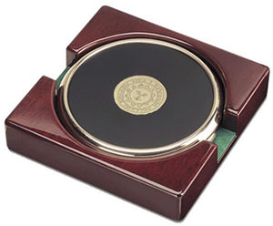 Burgundy piano wood stand holding two round black leather coasters with gold rim and gold engraved Bowdoin sun seal in center.