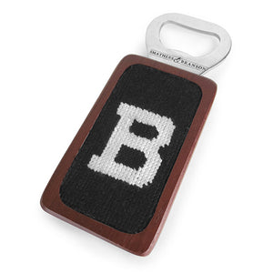 Rectangular wooden bottle opener with needlepointed inset with a white B on black field.