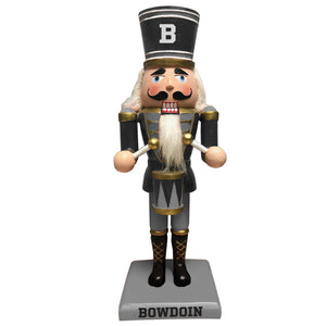 White-skinned nutcracker doll with black hat with B, black and grey uniform with gold accents, white hair, blue eyes, and drum. Base is grey with black BOWDOIN imprint.
