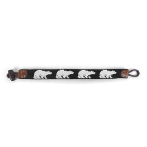 Flat view of needlepoint bracelet showing design of repeating polar bears on black background.