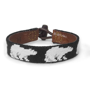 Needlepoint bracelet with design of reapeating polar bears on a black background. Leather backing and toggle clasp.