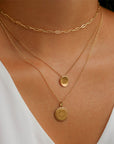 White woman wearing a plain gold chain necklace, a Bowdoin B Petite necklace, and a Bowdoin Seal Sunburst necklace.
