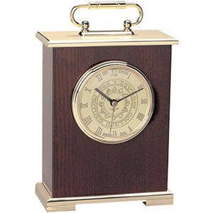 Small clock with gold tone base, top, handle, and dial. Dark piano wooden case. Dial is engraved with Bowdoin sun seal and has Roman numeral hour markers.