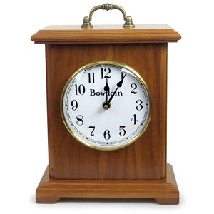 Simple bracket style mantel clock in light autumn finish with brass handle on top. Clock face is white with Arabic numeral hour markers and a Bowdoin wordmark under 12.