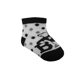 White socks with black and grey dots, black toes, heel, and cuff. Knit in polar bear in a B sweater, leaning on the letter B over top of foot.